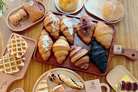 Nhìn từ trên xuống mẻ bánh trong ngày: croissant, bánh cuộn, waffle và bánh mì trên những khay gỗ khắc EMME, quanh khối gỗ số 413