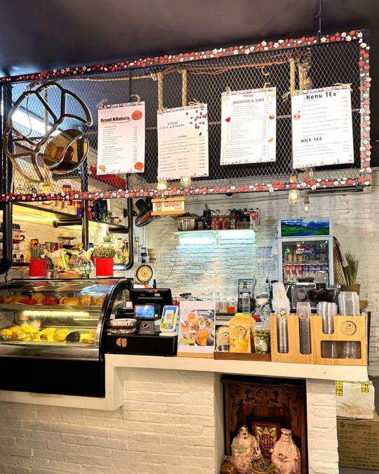 Quầy bánh với tủ kính bày bánh mì và bốn bảng giá treo bên trên