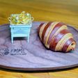 Croissant sọc socola trên đĩa gỗ khắc chữ EMME 413, bên cạnh là bộ bàn trà tí hon mạ vàng