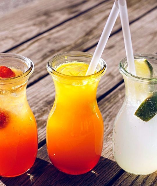 Ba ly nước ép trái cây màu đỏ, cam và vàng nhạt trên mặt bàn gỗ